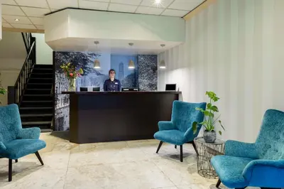 a man standing at a counter in a lobby with blue chairs at NH Centre Utrecht Hotel in Utrecht