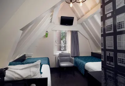 a room with two beds and a chair and a window at Singel Hotel Amsterdam in Amsterdam