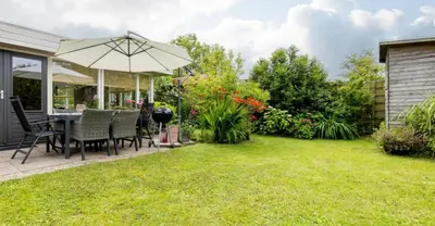 a backyard with a table and chairs and an umbrella at VT wonen stijl vakantiebungalow nabij zee, strand, bos en duinen voor 6 personen in Warmenhuizen