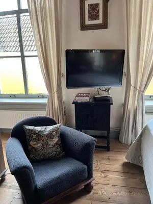 a living room with a chair and a flat screen tv at B&B De Kamer Hiernaast in Gouda