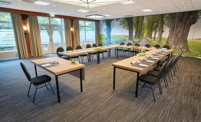 a conference room with tables and chairs and a tree at Amrâth Hotel Lapershoek Arenapark in Hilversum