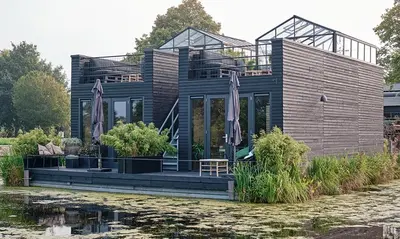a wooden house with a deck next to a body of water at GreenFloat Boskoop #2 Mica & Luca in Boskoop