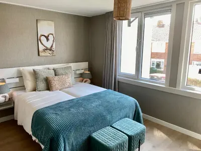 a bedroom with a bed with a blue blanket and a window at Glücklich am Meer Apartment Deluxe mit Wellnesszugang in Egmond aan Zee