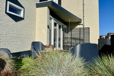 a house with two black chairs in the yard at Glücklich am Meer Apartment Deluxe mit Wellnesszugang in Egmond aan Zee