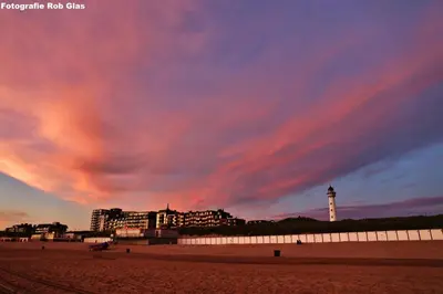 a beach with a building and a lighthouse under a cloudy sky at Glücklich am Meer Apartment Deluxe mit Wellnesszugang in Egmond aan Zee
