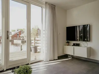 a living room with a tv and a large window at Waterside Escape with Easy Access in Uitgeest