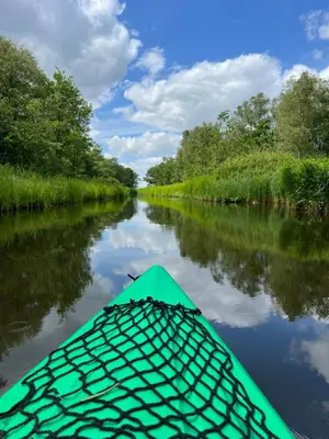 a green kayak on a river with trees at Huisje op de dijk in Kortenhoef