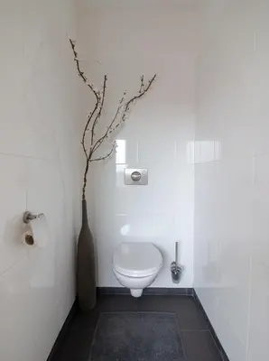 a bathroom with a toilet and a vase with a branch at ApartHotel Trendy by Urban Home Stay in Alkmaar