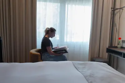a woman sitting in a chair reading a book in a hotel room at Boutique Hotel Herbergh Amsterdam Airport FREE PARKING in Badhoevedorp