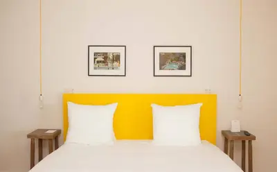 a bed with a yellow headboard and two tables at Vesper Hotel in Noordwijk aan Zee