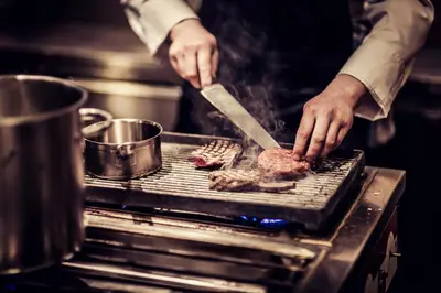a person cooking meat on a grill with a knife at Carlton Square Hotel in Haarlem