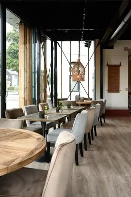 a restaurant with wooden tables and chairs and windows at Brasserie Spoorhuis Mijdrecht in Mijdrecht
