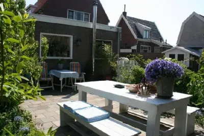 a patio with a white table and purple flowers at De Bollenschuur in Egmond aan Zee