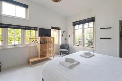 a white bedroom with a large bed and windows at Second Paradise for 2 adults and 2 children in Zandvoort