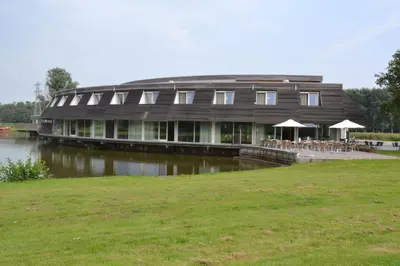 a large building with tables and umbrellas next to a lake at Fletcher Hotel - Resort Spaarnwoude in Velsen-Zuid