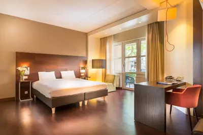 a bedroom with a bed and a desk and a window at Golden Tulip Ampt van Nijkerk in Nijkerk