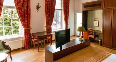 a living room with a tv and a desk and windows at Grand Hotel Karel V in Utrecht