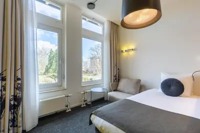 a hotel room with a bed and a chair and windows at Amrâth Berghotel Amersfoort in Amersfoort
