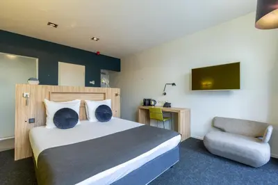 a bedroom with a bed and a chair and a television at Amrâth Berghotel Amersfoort in Amersfoort