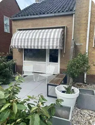a patio with awning and two chairs and a bench at Tiny beachhouse - free parking in Noordwijk