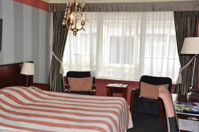 a bedroom with a bed and two chairs and a chandelier at Fletcher Hotel Restaurant Marijke in Bergen