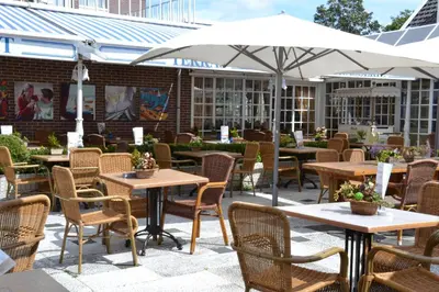 an outdoor patio with tables and chairs and an umbrella at Fletcher Hotel Restaurant Marijke in Bergen