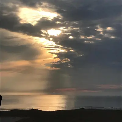 a cloudy sky over the ocean with the sun in the distance at Bed and Breakfast Kik en Bun in Katwijk aan Zee