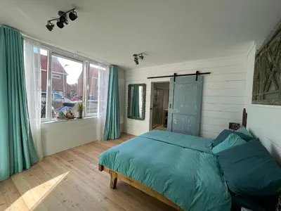a bedroom with a bed with blue sheets and a window at The Coast Beach House in Egmond aan Zee