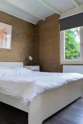 a white bed in a bedroom with a brick wall at -Casa Nova- nabij het meer, duinen en restaurants in Noordwijkerhout