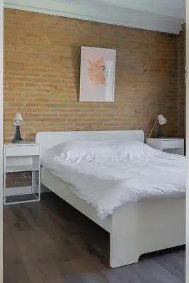a white bed in a bedroom with a brick wall at -Casa Nova- nabij het meer, duinen en restaurants in Noordwijkerhout