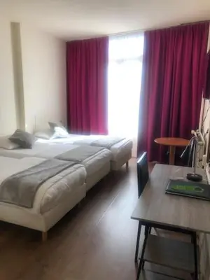 a bedroom with two beds with red curtains and a table at Delta Hotel City Center in Amsterdam