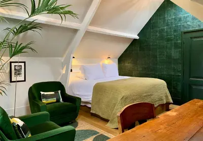 a bedroom with a bed and two green chairs at Boutique hotel Villa Trompenberg in Hilversum