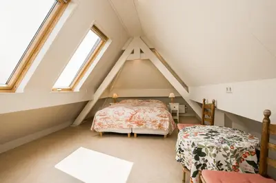 a attic bedroom with two beds and two windows at Villa de Duintop in Bergen aan Zee