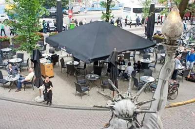 a group of people sitting at tables under a black umbrella at Hotel Prins Hendrik in Amsterdam