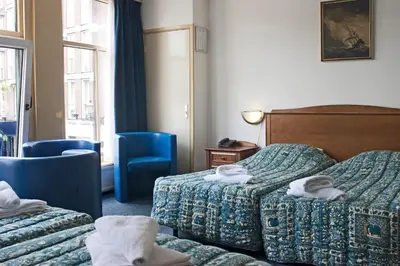a hotel room with two beds and blue chairs at Hotel Prins Hendrik in Amsterdam