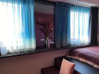 a bedroom with a bed and a window with blue curtains at Palace Hotel Zandvoort in Zandvoort