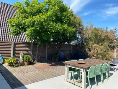a wooden table and chairs in a yard with a tree at White Sand Beach in Bergen aan Zee