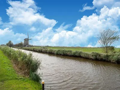 a river with a windmill in the middle of a field at Holiday home in Burgerbrug near the beach in Burgerbrug