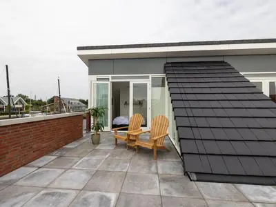 a house with a black roof and two chairs on a patio at Lakehouse I in Uitgeest