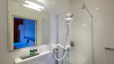 a white bathroom with a shower and a mirror at Hotel Aalders in Amsterdam