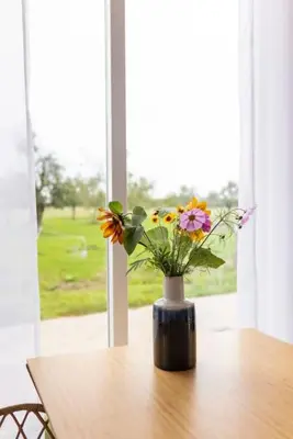 a vase with flowers sitting on a table in front of a window at De Boterhal - vakantiehuisje op natuurboerderij in Hem