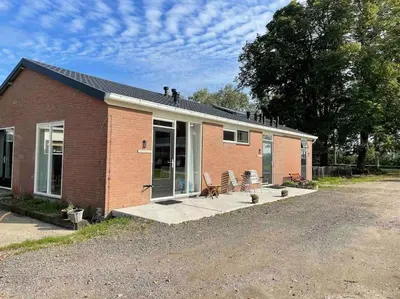 a red brick house with a porch and patio at Groepsaccommodatie op natuurboerderij Huize Blokland in Hem