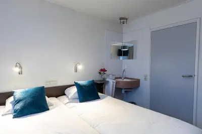 a bedroom with two beds with blue pillows and a sink at Hotel de Magneet in Hoorn