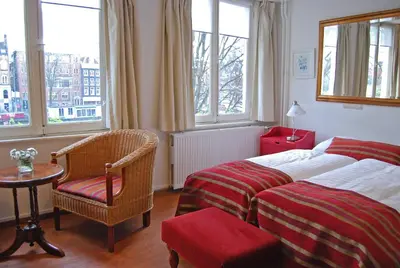 a hotel room with two beds and a chair and windows at Amsterdam House Hotel in Amsterdam