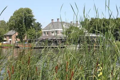a house on a bridge over a river with tall grass at Het Rechthuis in Uithoorn