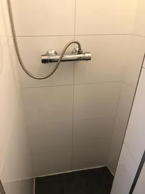a shower with a hose on a white wall at Romantisch Tiny Gardenhouse in beautiful garden in Zandvoort