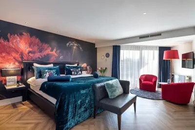 a bedroom with a large bed and a red chair at Van der Valk Hotel Leiden in Leiden