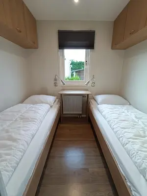 two beds in a small room with a window at Cozy chalet near Amsterdam at Camping Venhop in Berkhout
