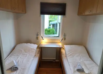 two beds in a small room with a window at Cozy chalet near Amsterdam at Camping Venhop in Berkhout