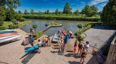 a group of people standing around a river with boats at Cozy chalet near Amsterdam at Camping Venhop in Berkhout